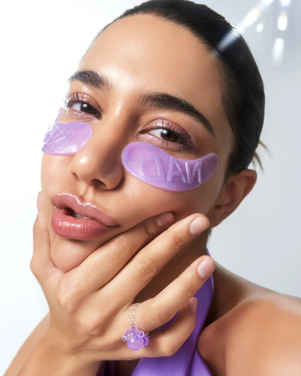 Woman wearing purple eye masks with 'L'OREAL' branding on a white background