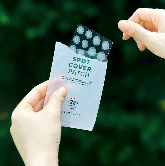 Hand holding a package of spot cover patches with a green blurred background