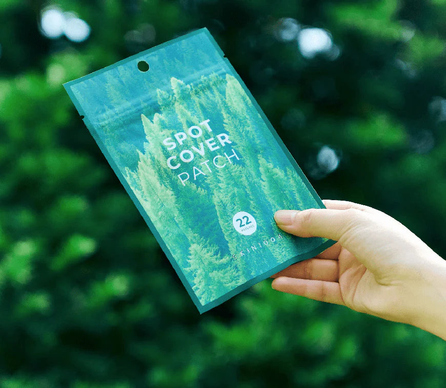 Hand holding a green package labeled 'Spot Cover Patch' against a blurred green background