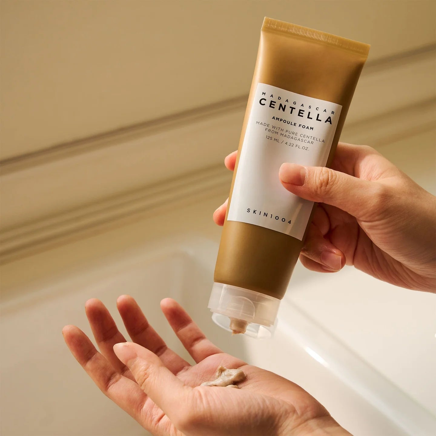 Hand holding a Skintoo tube of Madagascan Centella Astringent Foam over a sink.